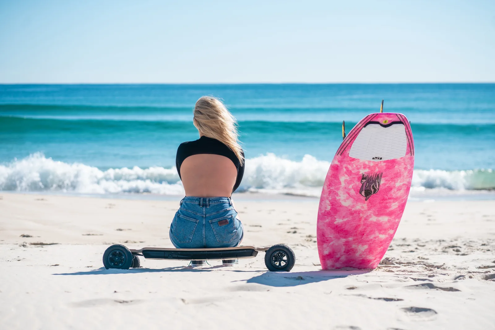 Del surf al skate - rider con una tabla de surf y un skate eléctrico Evolve en la playa